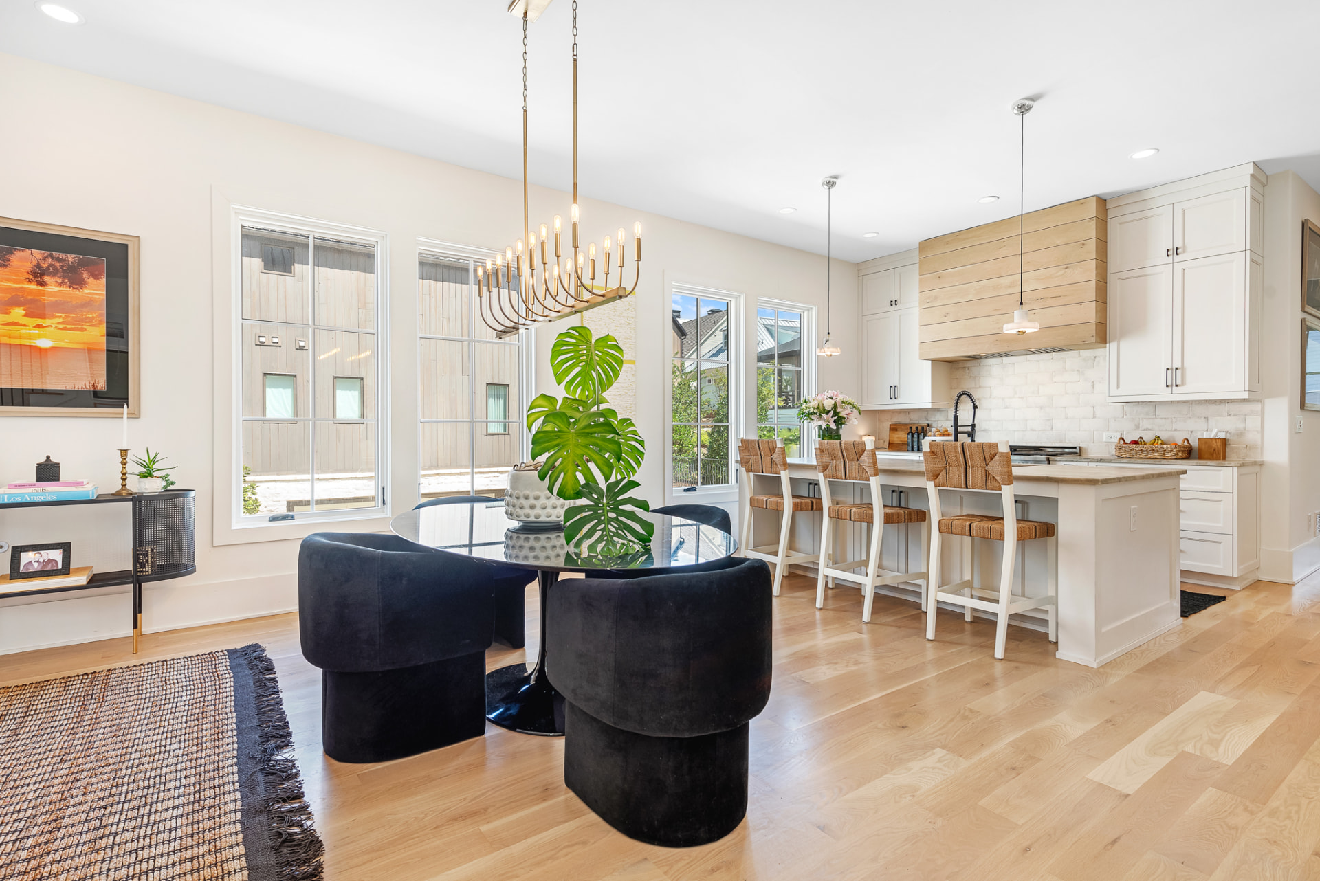 Dining area with black velvet chairs beside a white kitchen with woven counter stools
